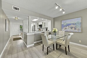 A modern kitchen with white cabinetry, a glass island, and a dining area with a glass table and four chairs.