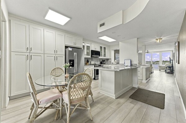 A modern kitchen with white cabinetry, a central island, and a dining area with wicker chairs.