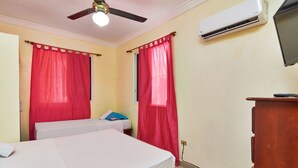 Une chambre d’hôtel avec deux lits, des rideaux rouges, un ventilateur de plafond, un climatiseur et un bureau en bois.