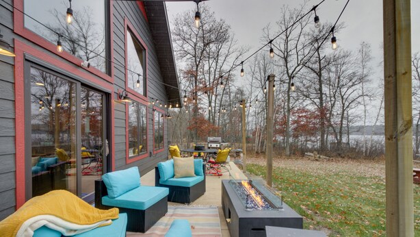 Un patio exterior con mobiliario, una chimenea y luces colgantes.