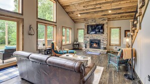 Un salón espacioso con chimenea de piedra, sofá de cuero y ventanas amplias que ofrecen vistas al exterior.