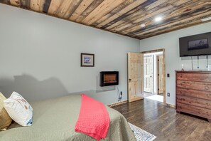 A bedroom with a bed, a television, a dresser, and a door leading to another room.