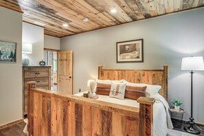 A bedroom with a wooden headboard, a bed with white bedding, a bedside table with a lamp, and a framed picture on the wall. - Modern Lakeside Chalet on Crow Wing Chain w/ Dock! (Nevis)