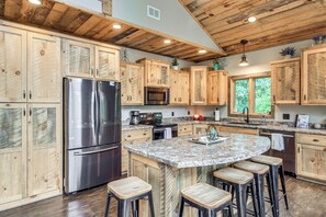 A kitchen with wooden cabinets, stainless steel appliances, a granite countertop, and bar stools.