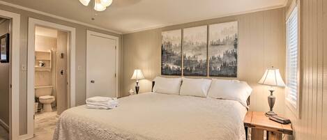 Un dormitorio con una cama grande, un ventilador de techo, una mesita de noche con lámpara y un cuadro en la pared.