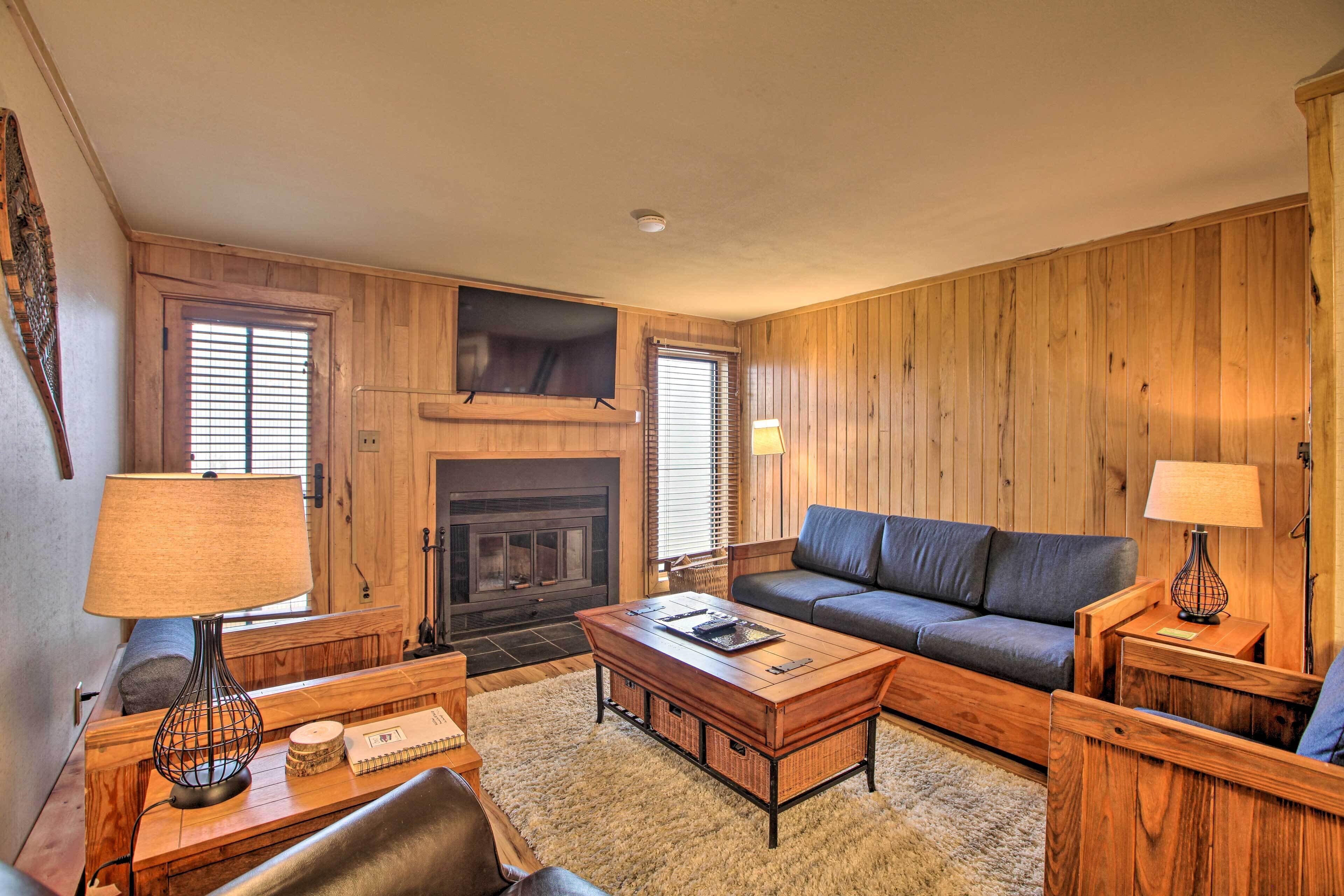 A cozy living room with a fireplace, wooden walls, a sofa, a coffee table, and two lamps.