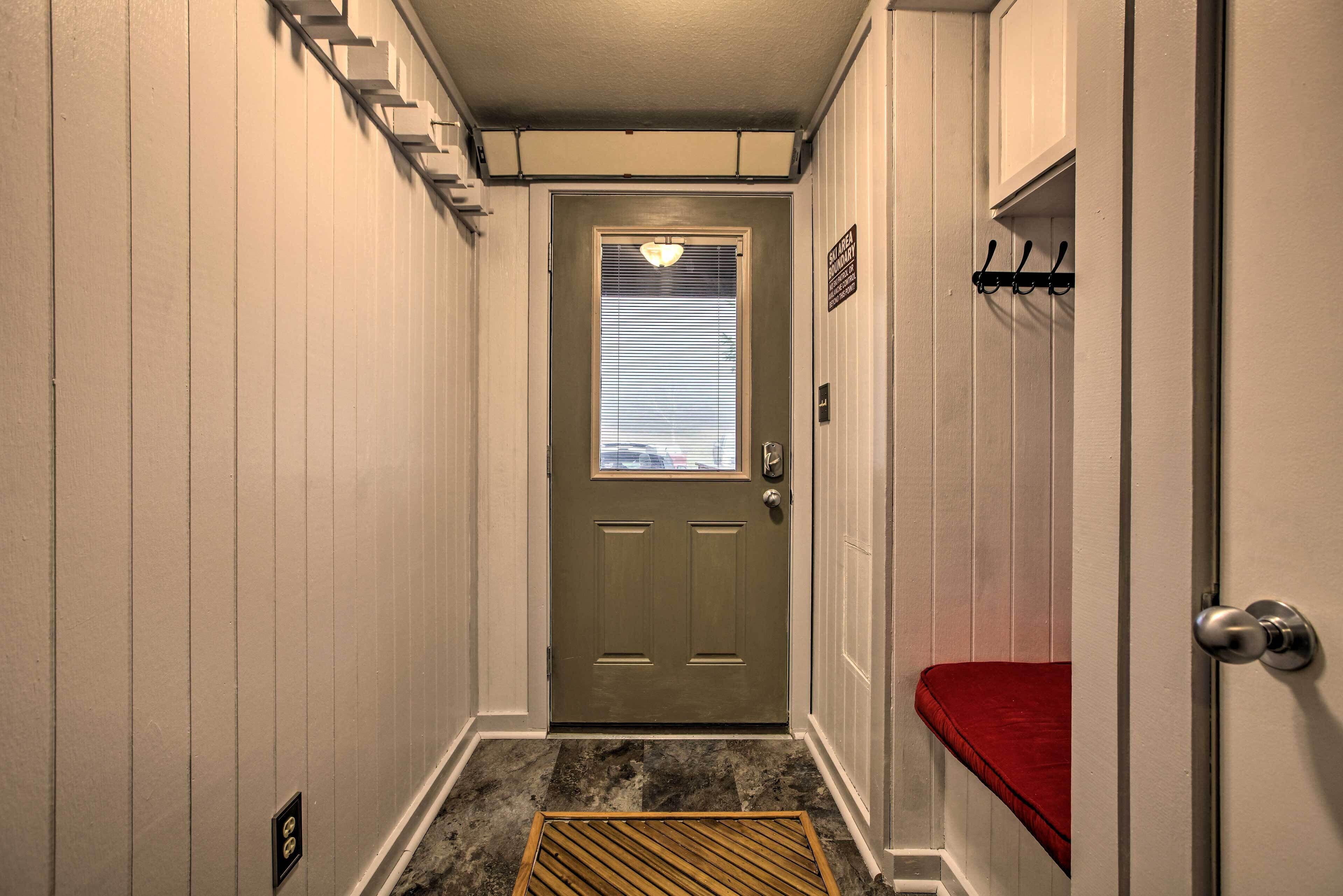 A narrow hallway with a wooden door at the end, a red bench, and a metal handrail on the right.