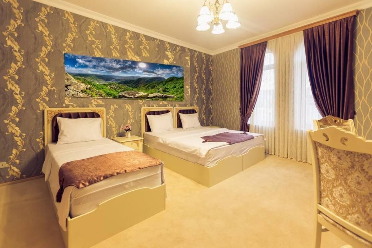 Ein Hotelzimmer mit zwei Betten, einem großen Landschaftsbild, einer Kristallleuchtre und einem klassischen Sessel.