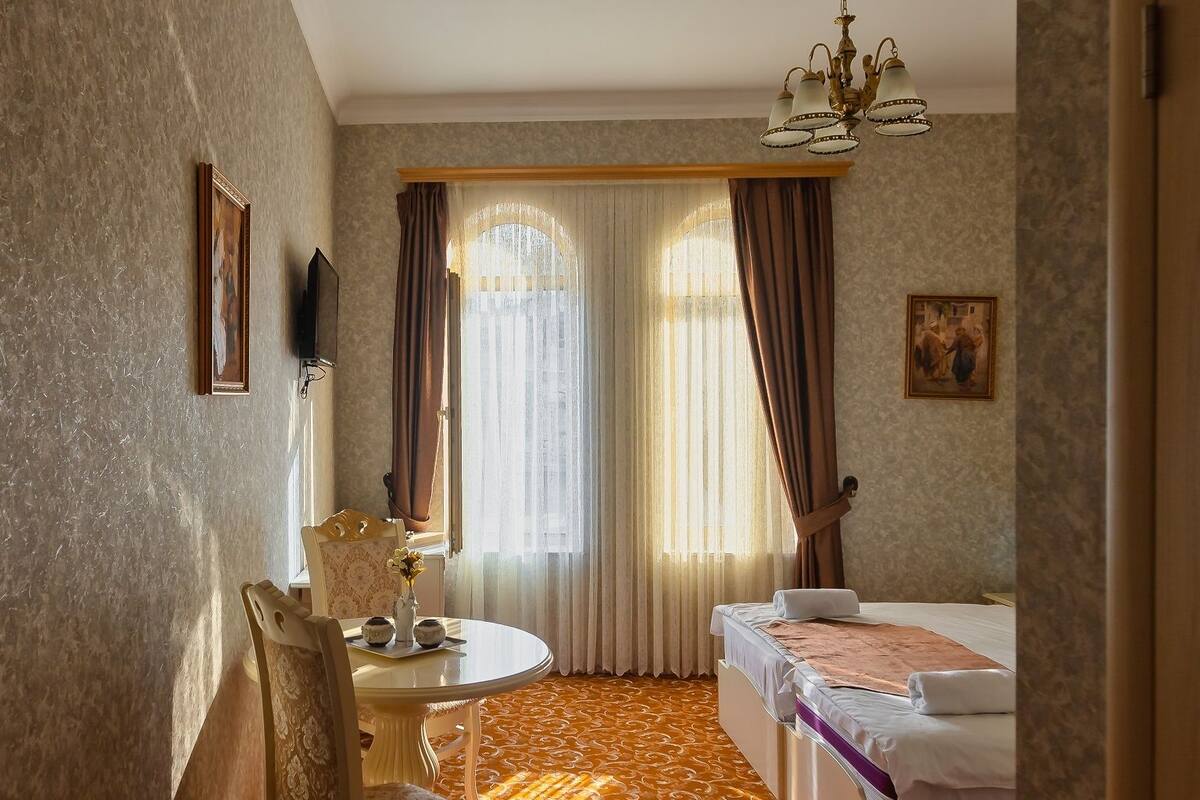 Ein Hotelzimmer mit einem Bett, einem Schreibtisch mit Stuhl, einem an der Wand befestigten Fernseher und einem gemusterten Teppich.