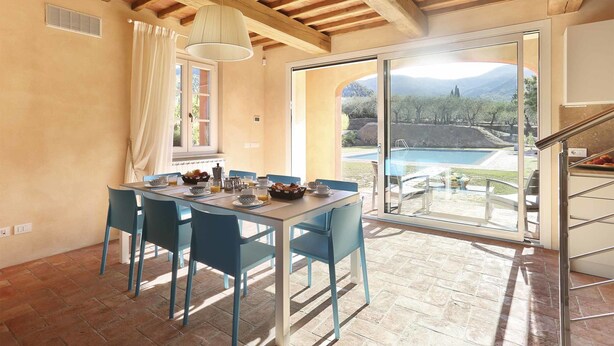A dining area with a table set for four, a large window with a view of a pool and mountains, and a wooden ceiling. - Villa in Colle Di Compito with 3 bedrooms sleeps 6 (Colle Di Compito)