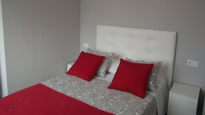 Una camera da letto con un letto, due cuscini rossi, un comodino bianco e una coperta a letto grigia con motivo.