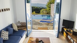 Un salon comprenant un canapé, une table basse, un meuble pour la télévision et donnant sur une piscine extérieure et un paysage verdoyant.