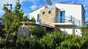 Une maison moderne à deux étages, dotée d’une façade en pierre, d’une antenne parabolique et d’un balcon avec des garde-corps bleus.
