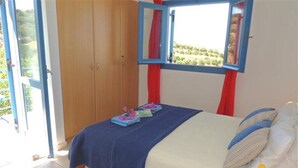 Une chambre à coucher avec un lit, une fenêtre avec des rideaux, une armoire et une vue sur la verdure à l’extérieur.