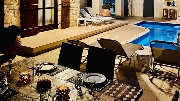 Un edificio de dos pisos con fachada de piedra, piscina y mobiliario exterior.