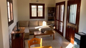 Una sala de estar con un sofá, una mesa de centro, un televisor, una estantería y una puerta con paneles de vidrio.