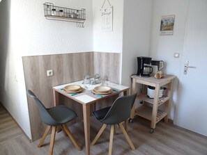 Una cocina pequeña y moderna con una mesa de comedor, dos sillas, una cafetera y una estantería con utensilios de cocina.