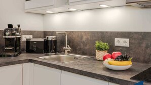 A modern kitchen with a coffee machine, a kettle, and a sink. There is a fruit bowl with apples and bananas on the counter. - Holiday Villa Waldstraße Whg. 16 - Holiday Villa Waldstraße Whg. 16 (Heringsdorf)