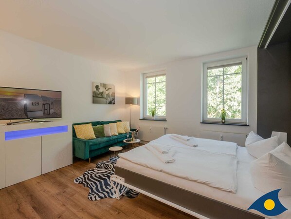 A modern bedroom with a large bed, a green sofa, a flat-screen TV, and two windows.
