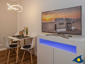 A modern dining area with a TV displaying beach chairs, a table with wine glasses, and a unique ceiling light fixture.