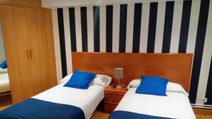 A hotel room with two beds, each with blue bedding and white pillows. There is a wooden wardrobe and a striped wall behind the beds. - Aldatzeta Ostatua (Bermeo)