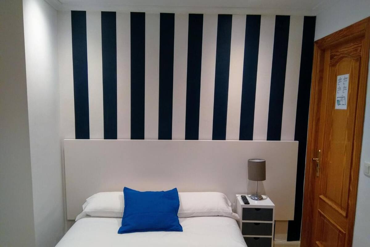 A hotel room with a bed, a nightstand, a lamp, and a door.