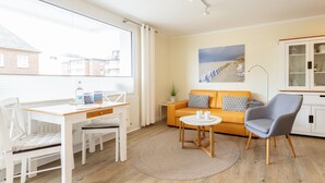 Un salon moderne avec une table blanche, un canapé et un fauteuil gris. Un tableau est accroché au mur, et il y a un meuble avec des portes en verre.
