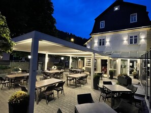 An outdoor patio area with tables and chairs, a covered seating area, and a building in the background. - Hotel - Gasthof Hüttensteinach (Sonneberg)