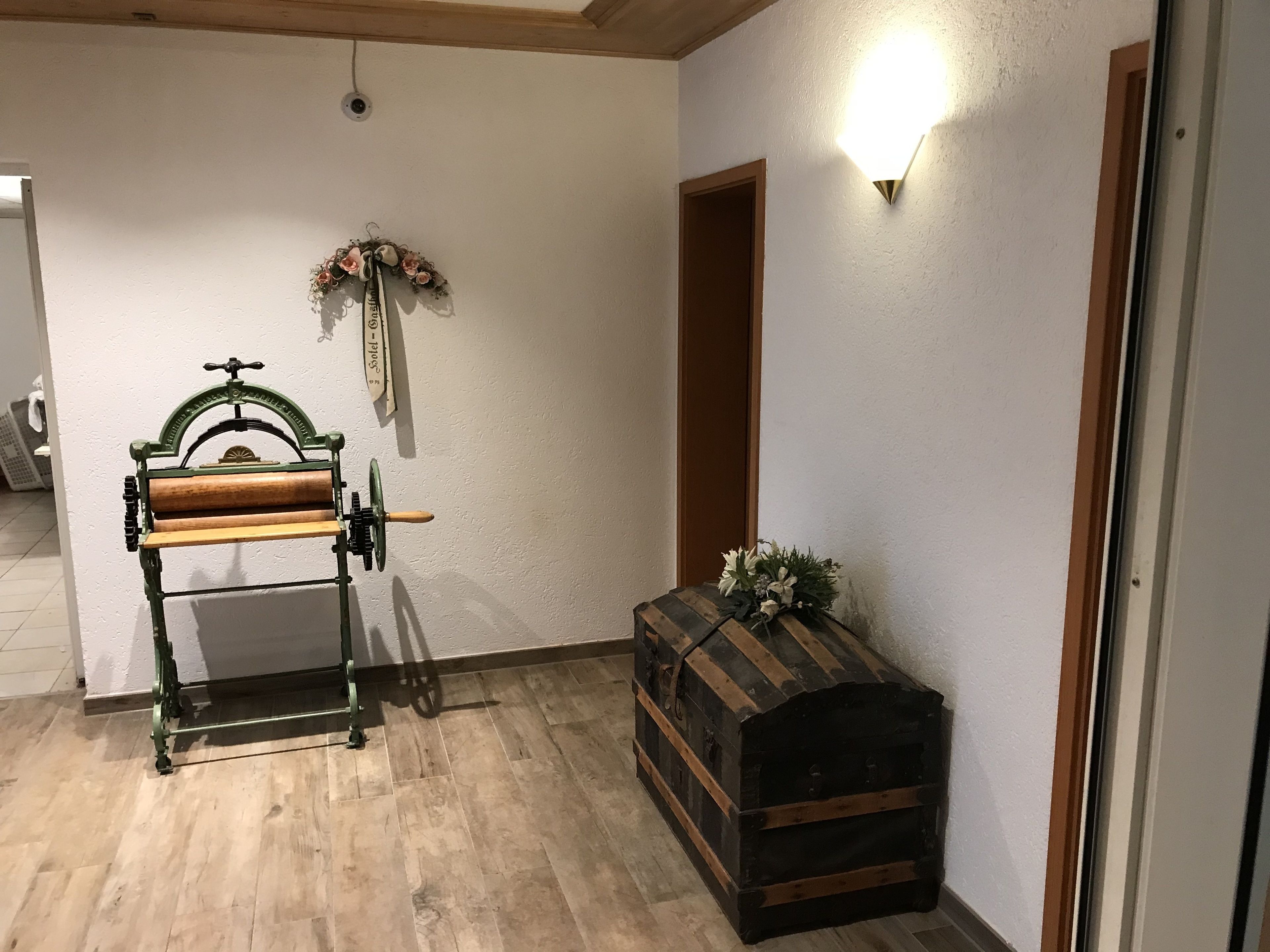 Habitació amb una banca de fusta, una corona decorativa, una làmpada de paret i un arca antic.