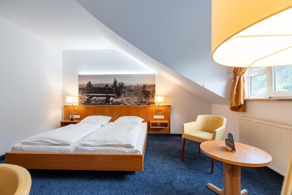 Una habitación de hotel con una cama, una silla, una mesita y un cuadro en la pared.