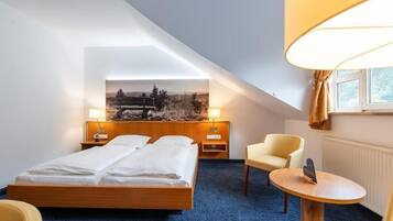Una habitación de hotel con una cama, una silla, una mesita y un cuadro en la pared.