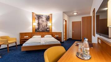 Ein Hotelzimmer mit einem Bett, einem Schreibtisch mit einer Wasserflasche, einem Stuhl und einem Bild an der Wand.