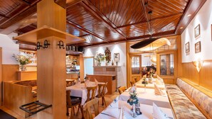 A restaurant with wooden ceiling beams, white tablecloths, and a long bench along the wall.