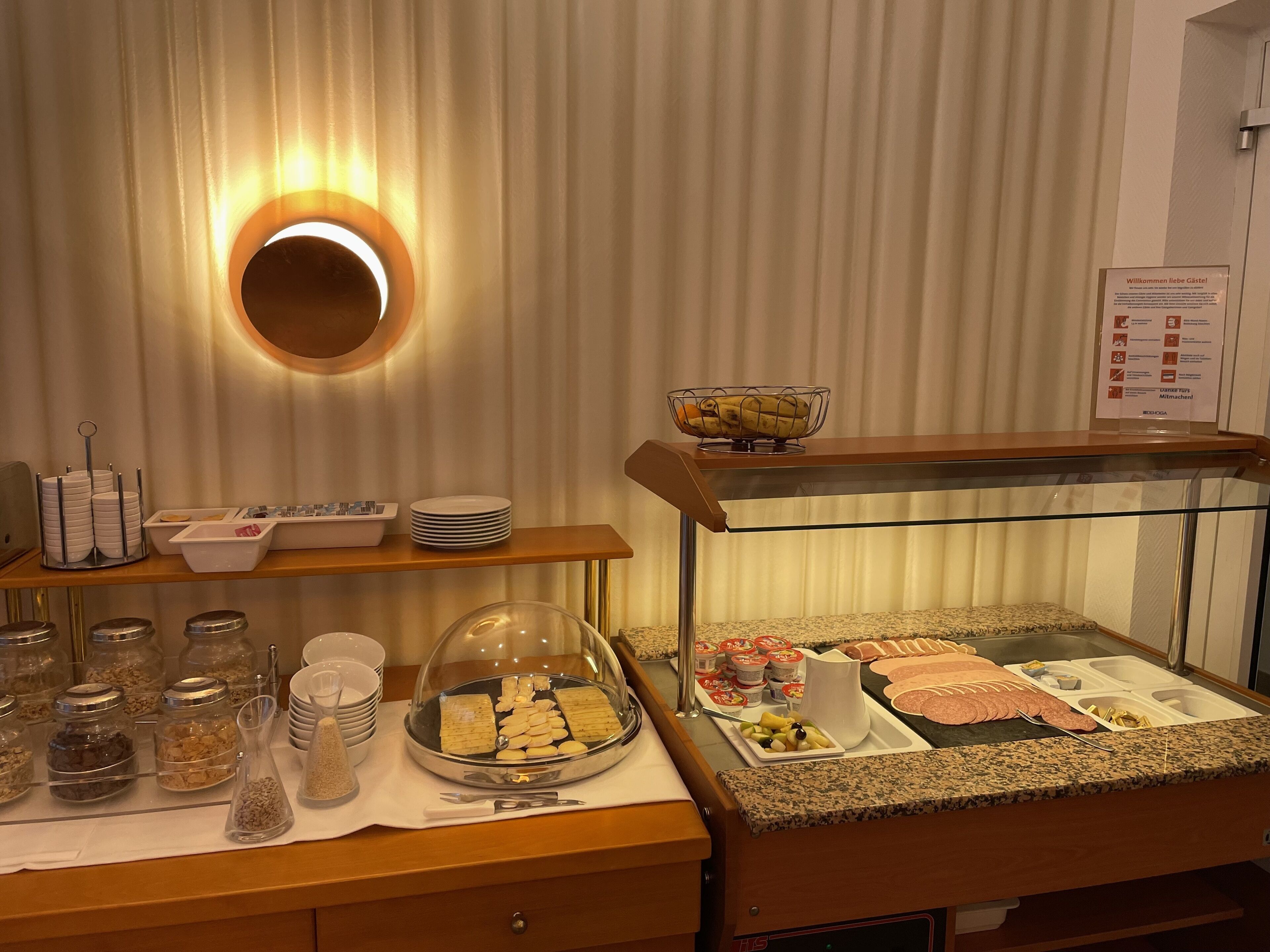 Ein reichhaltiges Buffet mit verschiedenen Speisen und Beilagen, eine Glastheke und ein Schild mit Text in einer Fremdsprache.