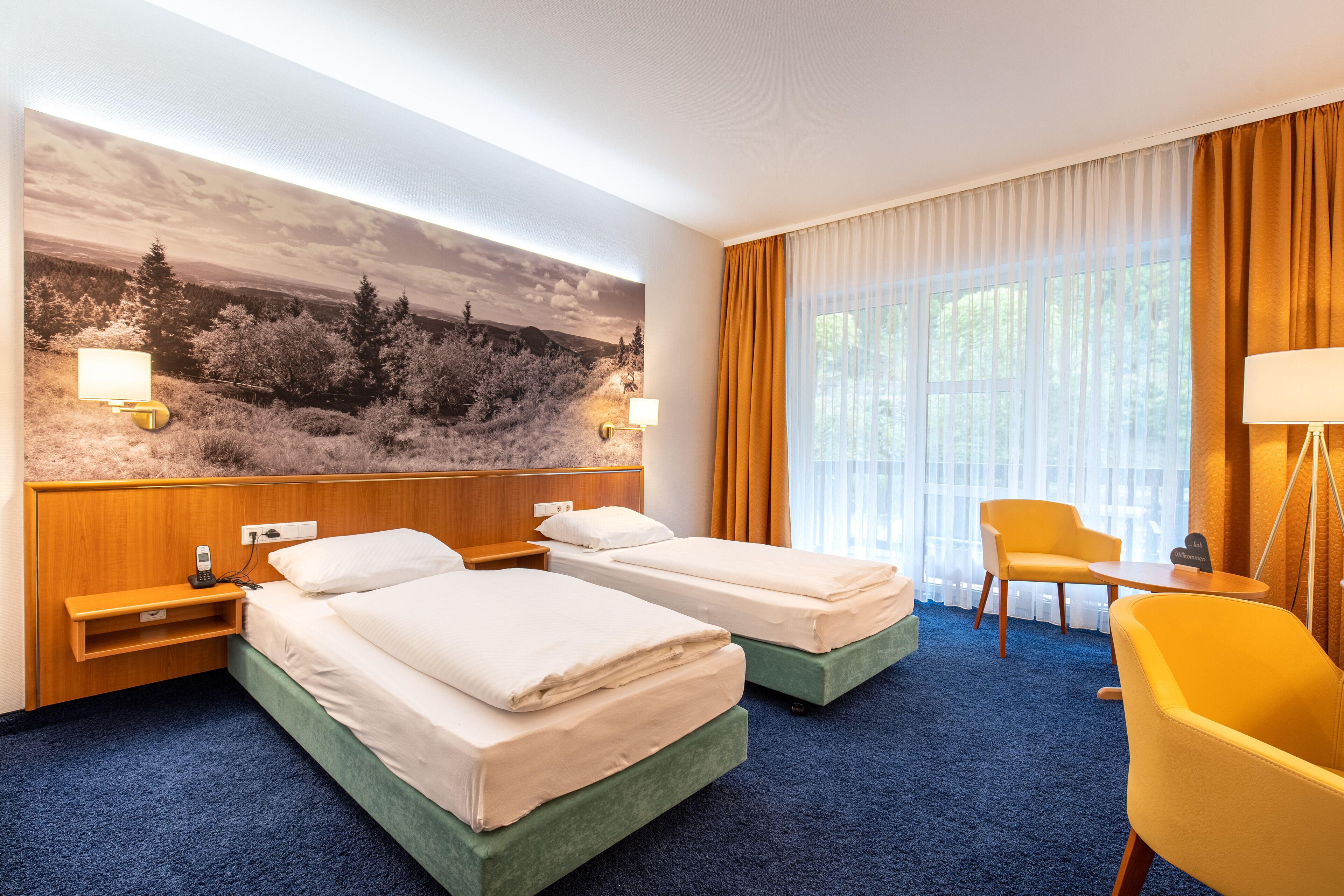 A hotel room with two beds, a desk, a chair, and a large window with curtains.