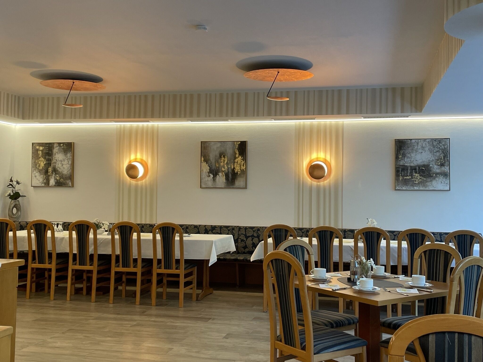 Un comedor con mesas largas, sillas e iluminación instalada en la pared.