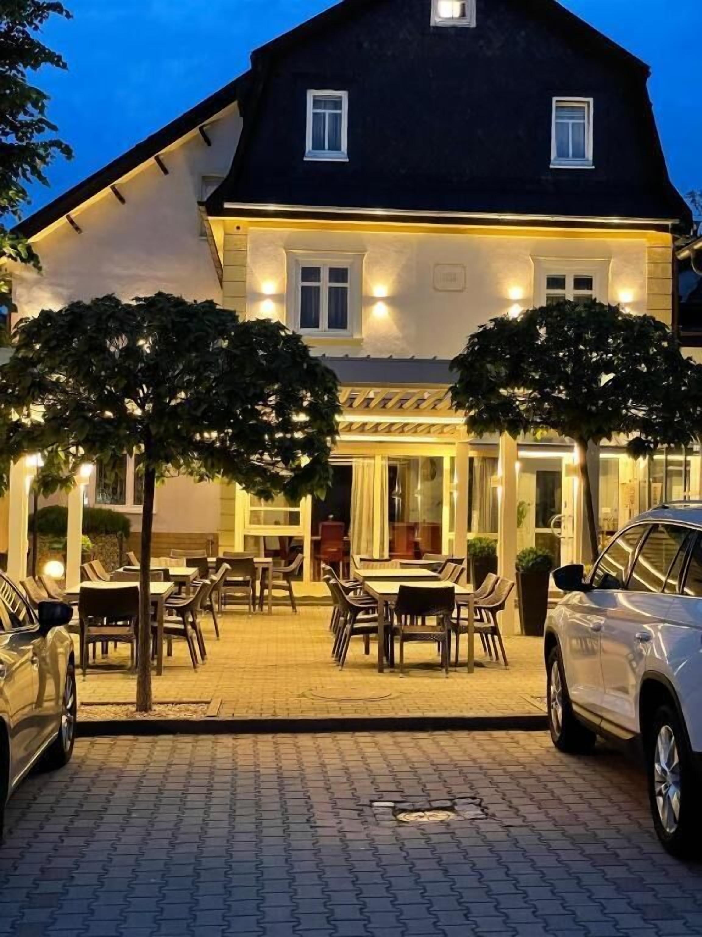 A building with a paved entrance, outdoor seating area, and a car parked in front.