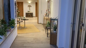 A hallway with wooden flooring, a central seating area with a table and chairs, and a decorative ceiling light.