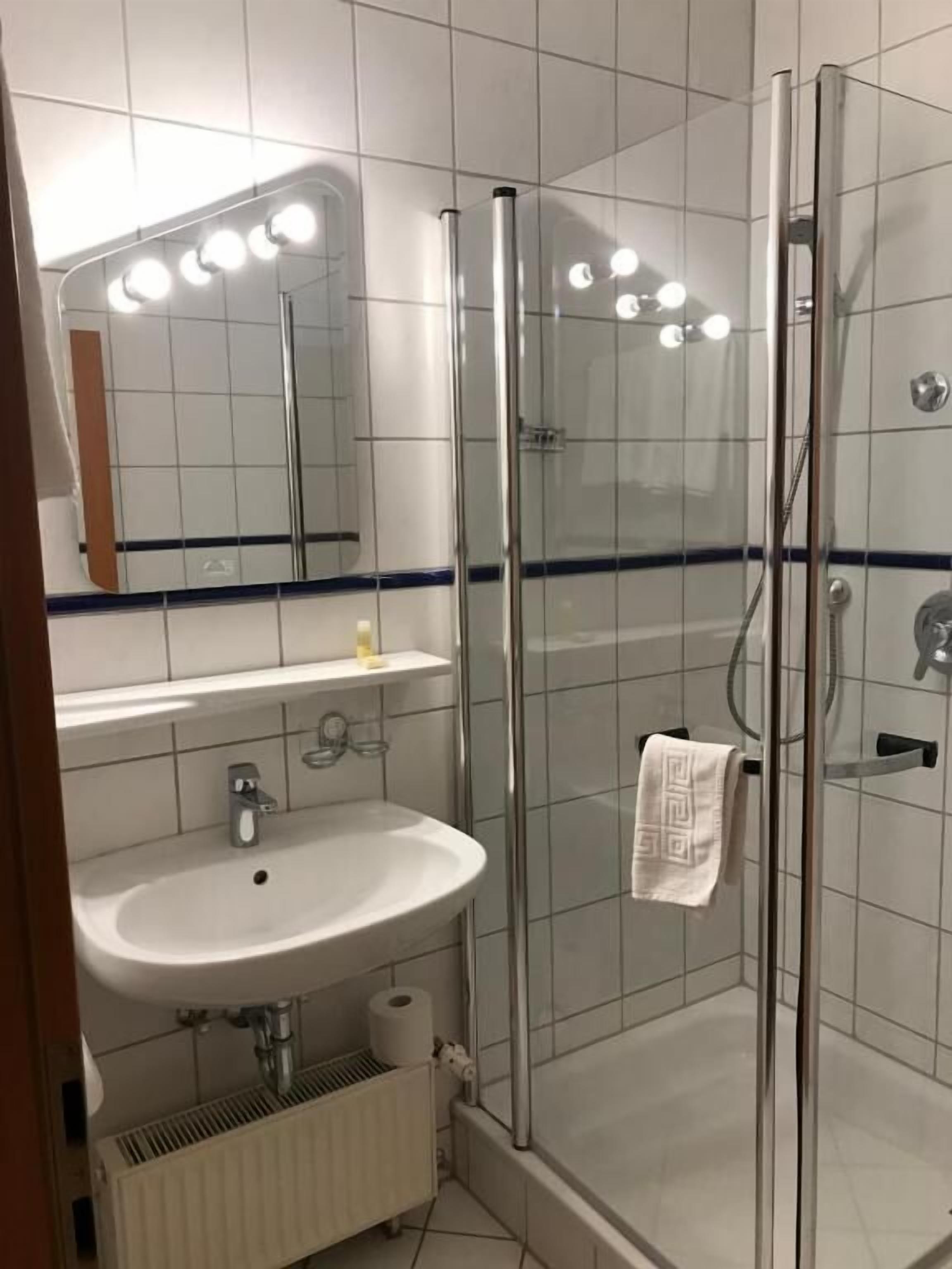 A modern bathroom with a glass-enclosed shower, a white sink, and a mirror with lights above it.