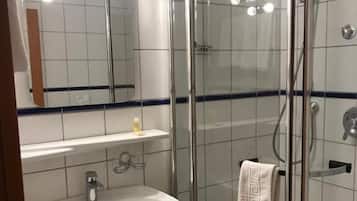 A modern bathroom with a glass-enclosed shower, a white sink, and a mirror with lights above it.