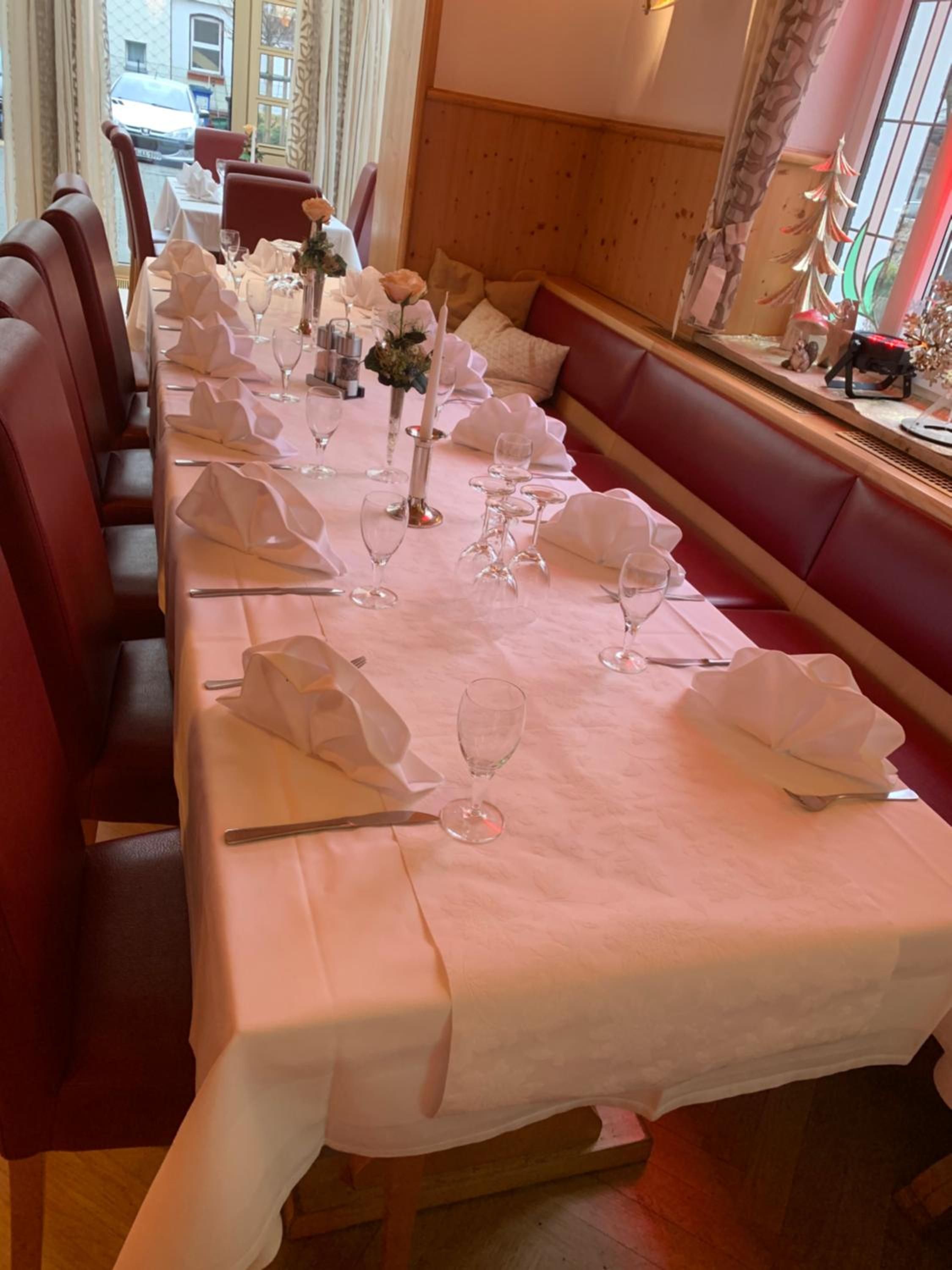 A long dining table set with white tablecloths, glassware, and folded napkins, flanked by red upholstered benches.