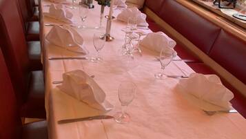 A long dining table set with white tablecloths, glassware, and folded napkins, flanked by red upholstered benches.