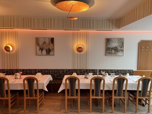 A dining area with multiple tables and chairs, wall-mounted light fixtures, and artwork. - Hotel - Gasthof Hüttensteinach (Sonneberg)