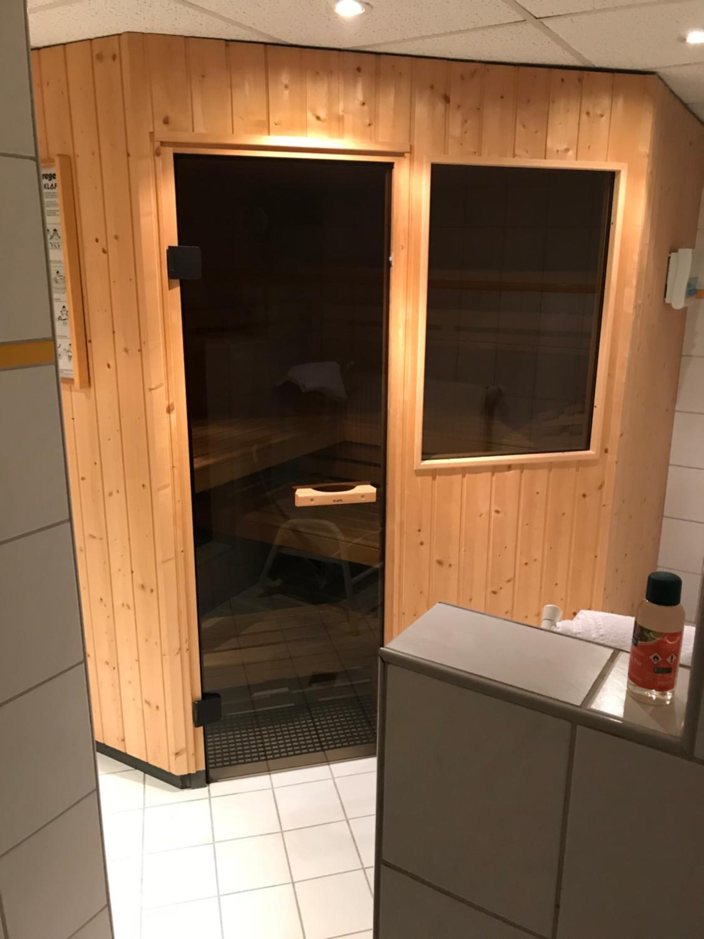 Una stanza sauna con pareti in legno e una porta in vetro, un piccolo lavandino e una bottiglia d'olio sul ripiano.