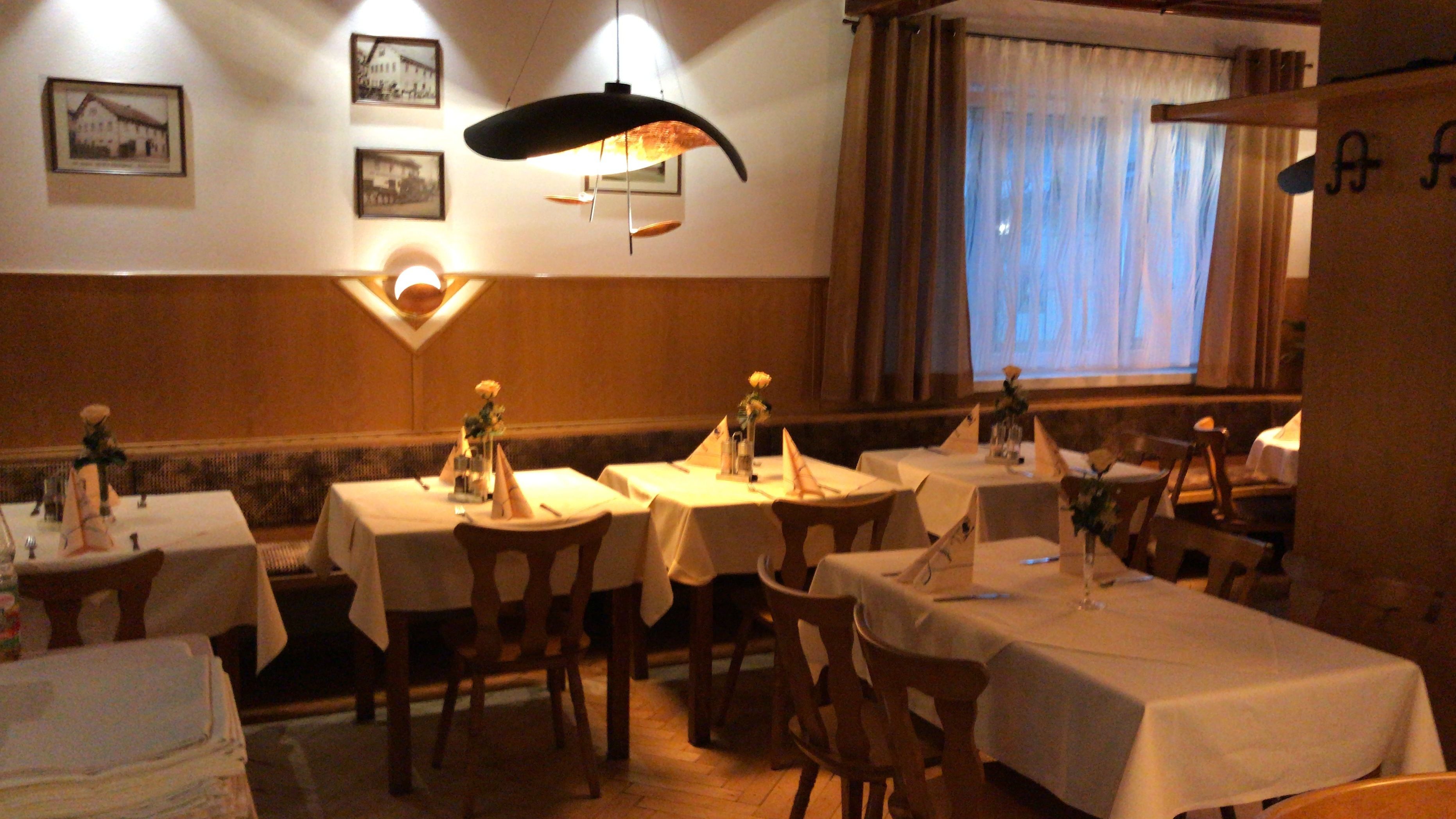 Un restaurante con varias mesas, cada una con un mantel blanco. Hay cuadros enmarcados en la pared sobre las mesas.