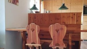 Ein Essbereich mit Holzbänken und -stühlen, einem Holztisch und einer grünen Pendelleuchte.