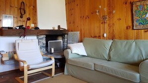 Ein gemütliches Wohnzimmer mit Kamin aus Stein, Holzwandverkleidung, einem weißen Sessel und einem grünen Sofa.