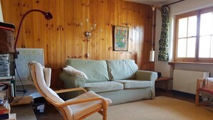 Ein gemütliches Wohnzimmer mit Holzwand, einem grünen Sofa, einem Holzstuhl, einer Lampe und einer Heizung.