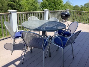 Eine Terrasse mit einem runden Metalltisch und Stühlen, einem Grill und einem Holzgeländer.