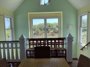 Ein Essbereich mit Holztisch und -stühlen, einer Bank und Blick auf einen Wald durch große Fenster.